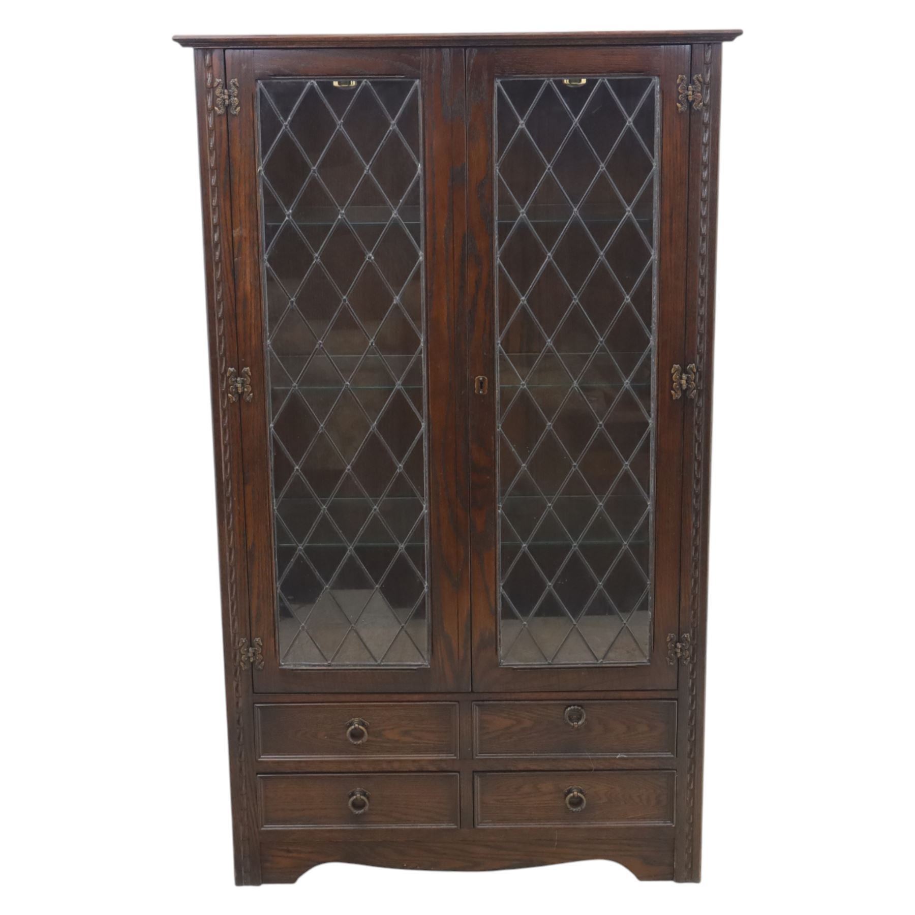 Mid 20th century oak display cabinet, the moulded rectangular cornice above a pair of leaded glazed doors with diamond lattice glazing, enclosing adjustable shelving, the lower section fitted with four short drawers with brass ring handles, flanked by chamfered uprights with carved leaf detail