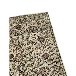 Persian Kashan ivory ground carpet, central medallion decorated with sixteen arranged palmette motifs, within a field decorated with swirling leafy branches and stylised plant motifs, the main border decorated with matching swirling pattern, within floral pattern guard stripes 