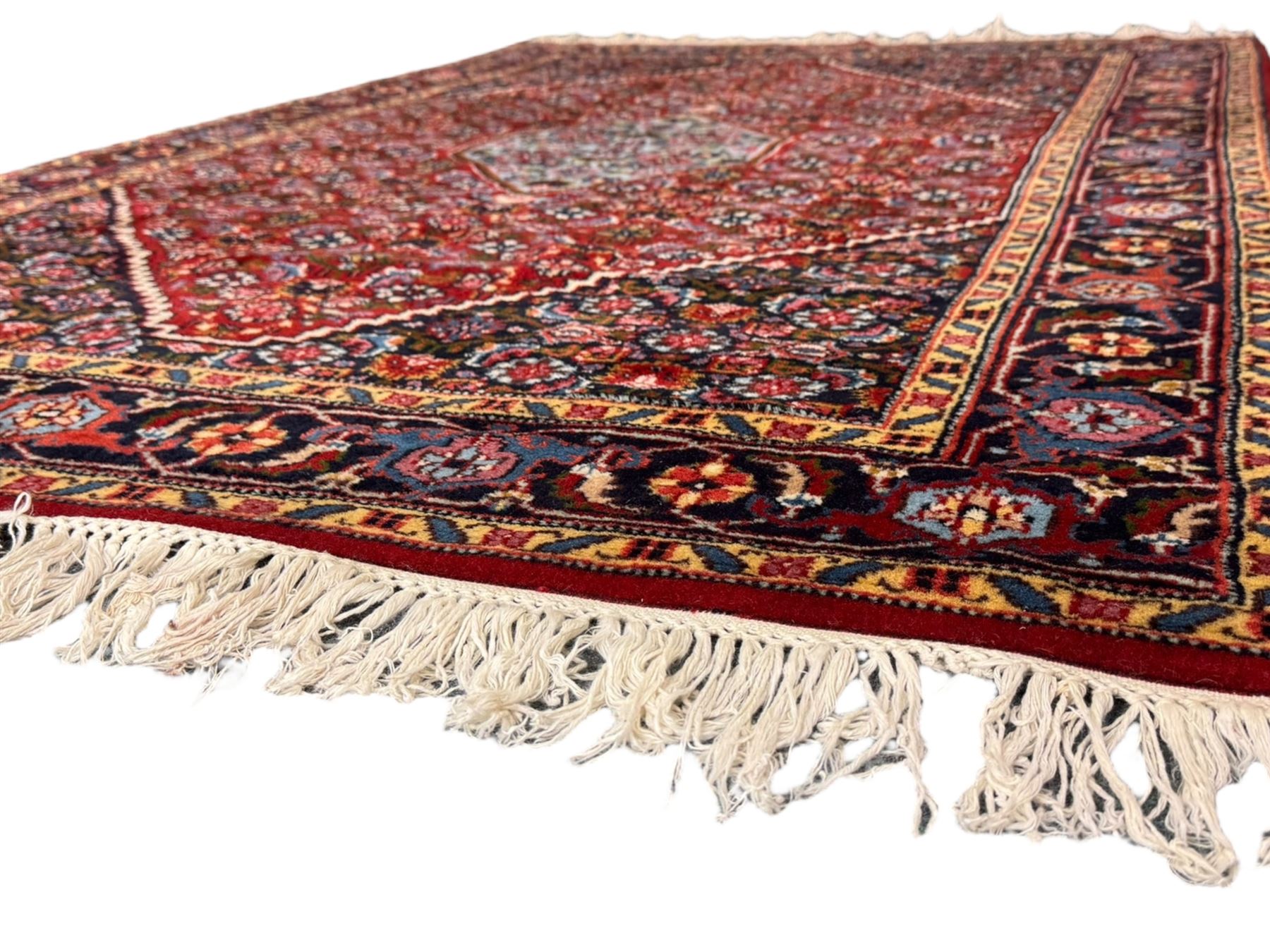 Persian crimson ground rug, central light blue lozenge medallion with floral motifs, the densely decorated crimson field filled with repeating flower heads and trailing leafy vines, the black and red border with interlacing foliate patterns and floral cartouches, surrounded by guard stripes