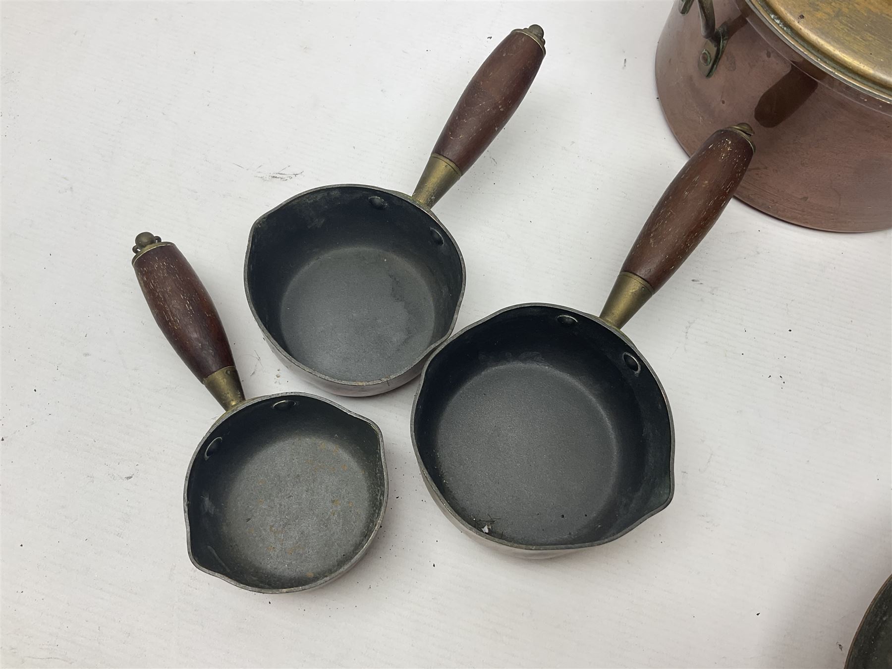 Four Victorian copper moulds, together with a graduating set of copper pans with wooden handles and finials to covers, largest pan 