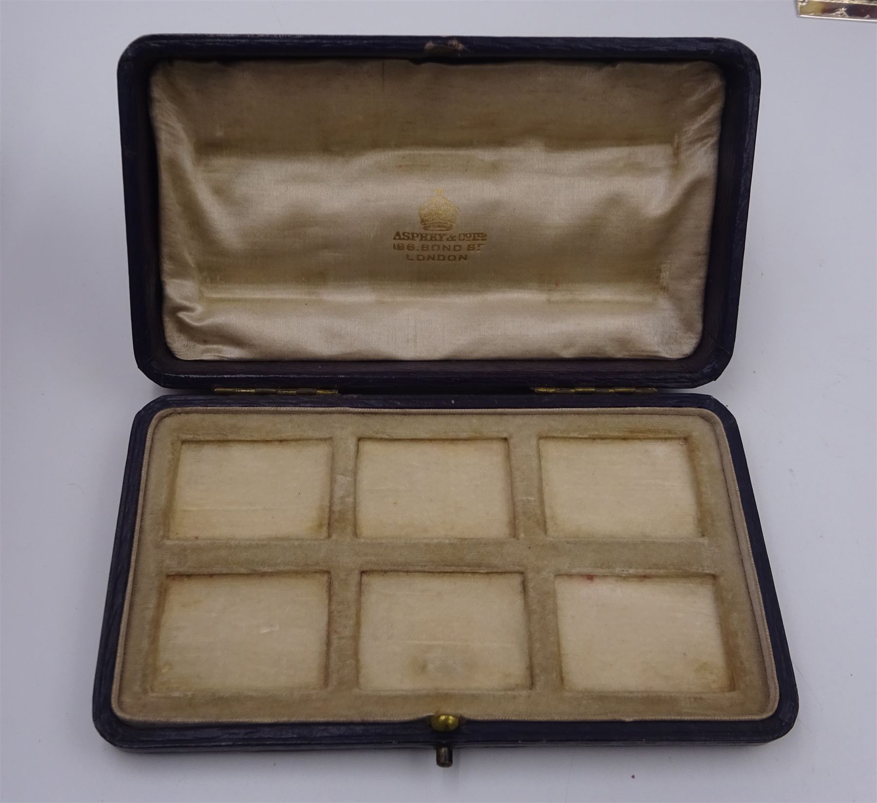 Set of six early 20th century silver mounted tortoiseshell place card holders by Asprey, the rectangular silver reed and ribbon frame bordering a central tortoiseshell panel inlaid with a silver floral motif, upon an oblong foot, hallmarked Asprey & Co Ltd, London 1913, H3cm, contained within a tooled leather fitted case with velvet and silk lined interior 