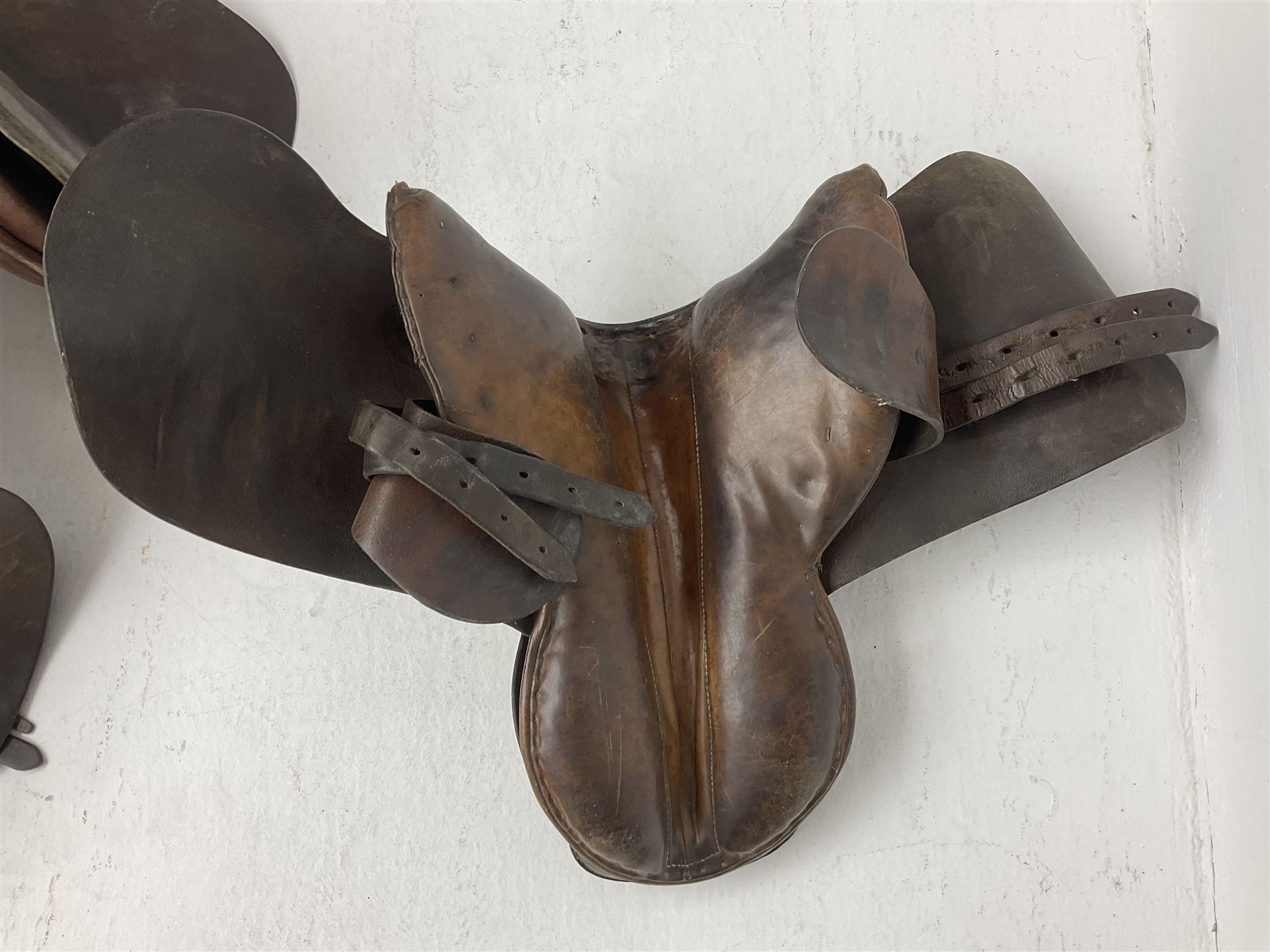 Collection of nine saddles, mainly havana leather to include a racing saddle and a Goodwin saddle, some with stirrups and leathers 