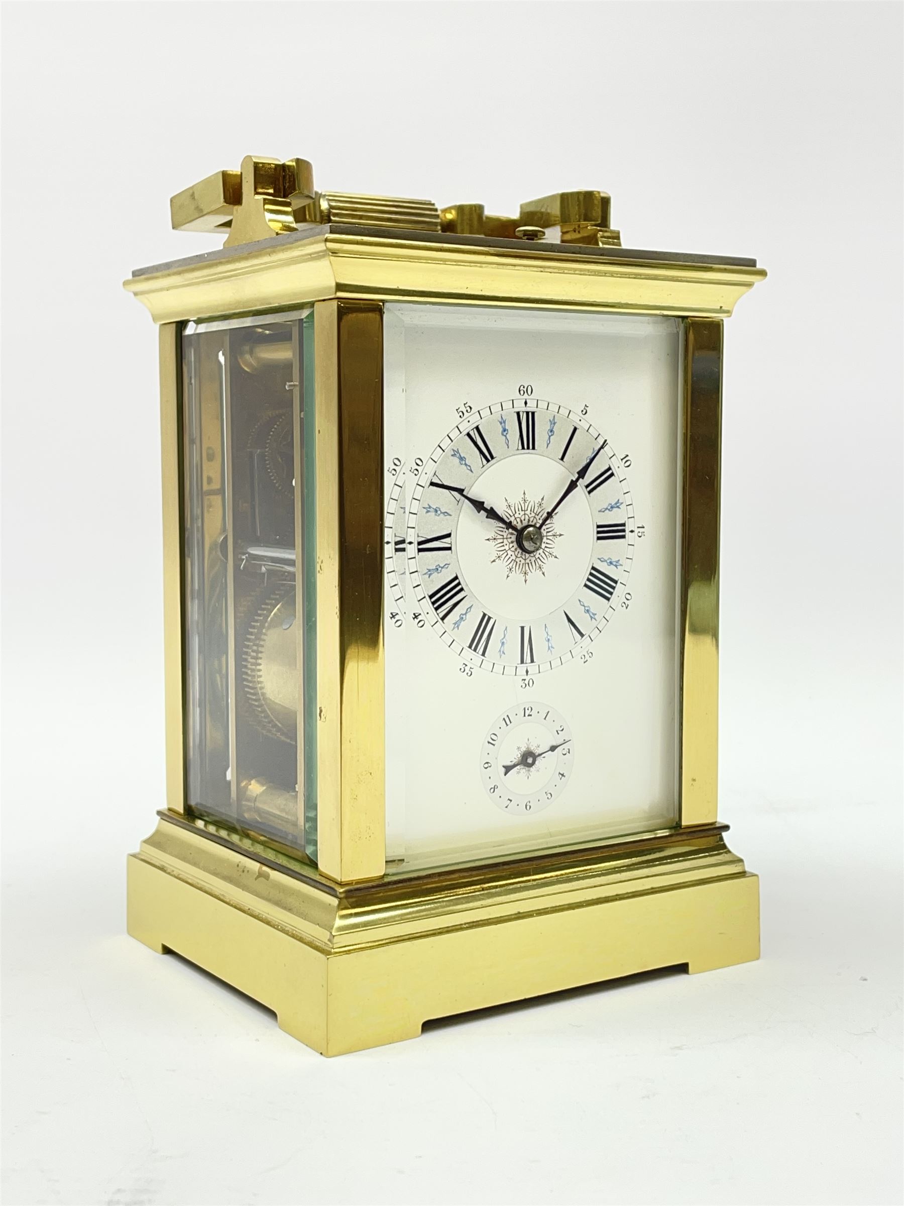 Early 20th century brass and bevelled glass repeater carriage clock with alarm, the angular and cylindrical ribbed handle and repeater button over stepped cavetto cornice, white enamel Roman dial with Arabic subsidiary alarm set dial, twin train eight day movement striking the hours and half on coil, separate alarm mechanism train, stepped moulded and plain faced base, with leather travelling case