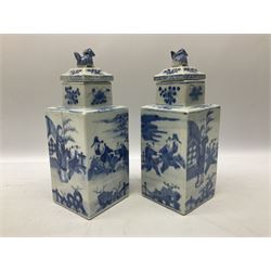 Pair of Chinese blue and white jars and covers of square form, decorated with figures in garden settings, the covers with foo dog finials, H21.5cm