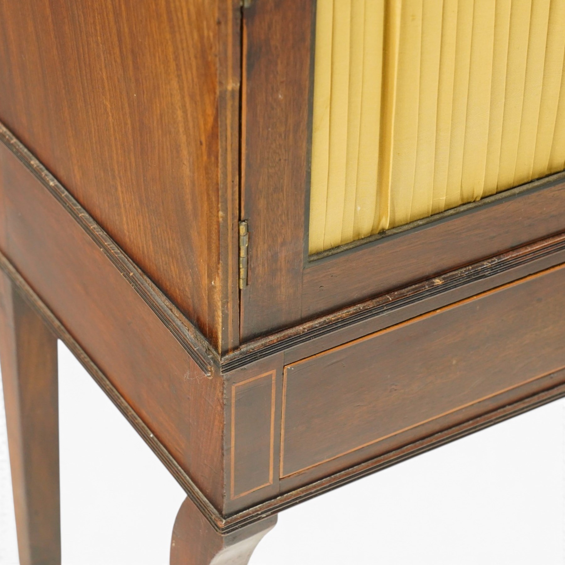 Regency period mahogany waterfall-bookcase chiffonier, the raised back with two open shelves supported by central ring-turned pilasters, fitted with twin doors with sage-green pleated fabric facias, over two drawers with satinwood stringing, raised on front sabre supports
