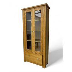 Light oak bookcase display cabinet, projecting square cornice over glazed double doors enclosing three adjustable shelves, single drawer base, on stile supports