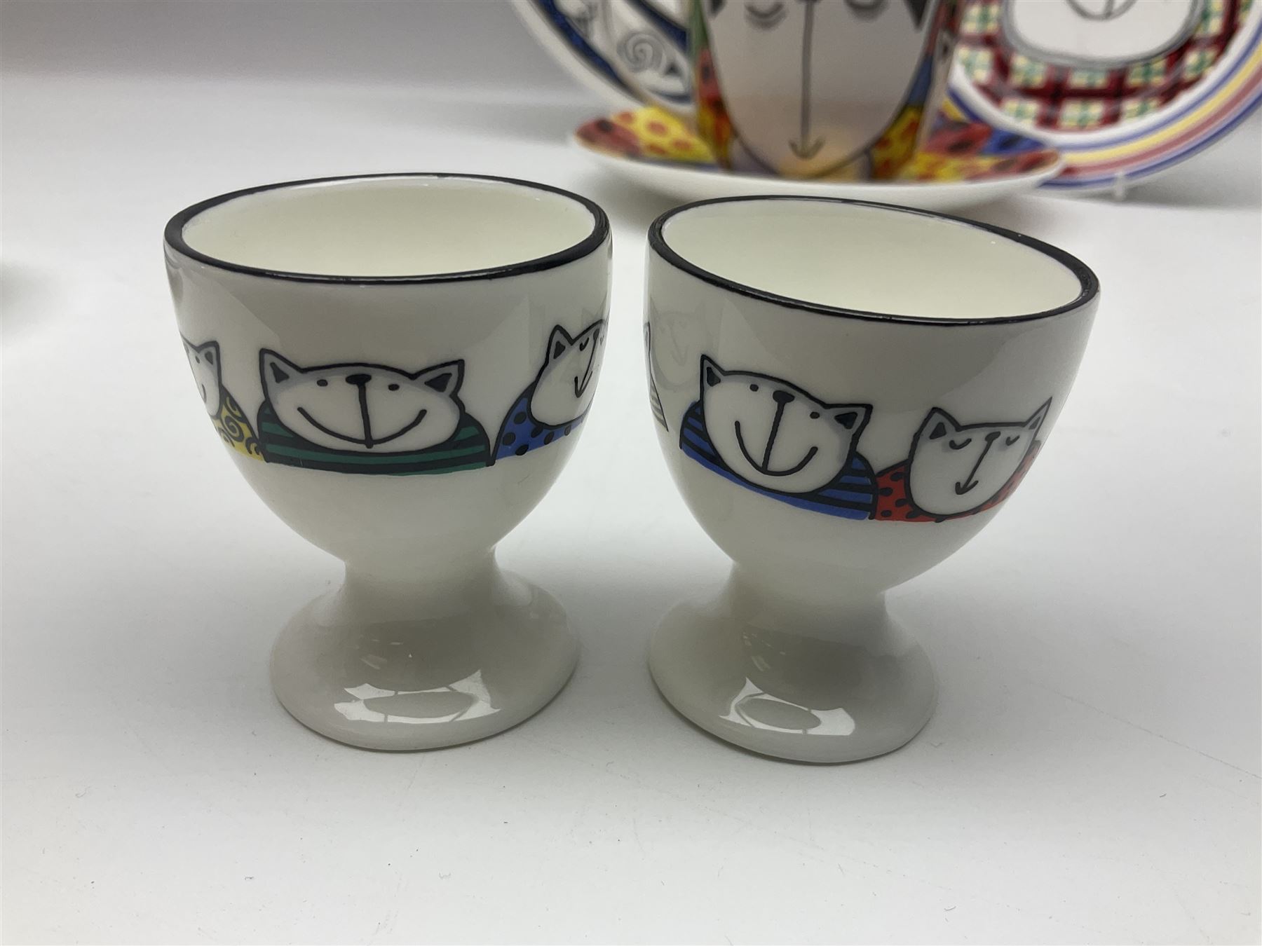 Modern studio pottery by Josie Firmin, to include cup and saucer, three espresso cups and saucers, pair of egg cups etc, each hand painted with varying cartoon cat designs