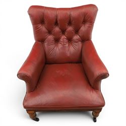 Early 20th century style oxblood red leather Chesterfield armchair, deep buttoned shaped back over padded scroll arms and loose seat cushion, raised on turned mahogany front supports with brass caps and castors