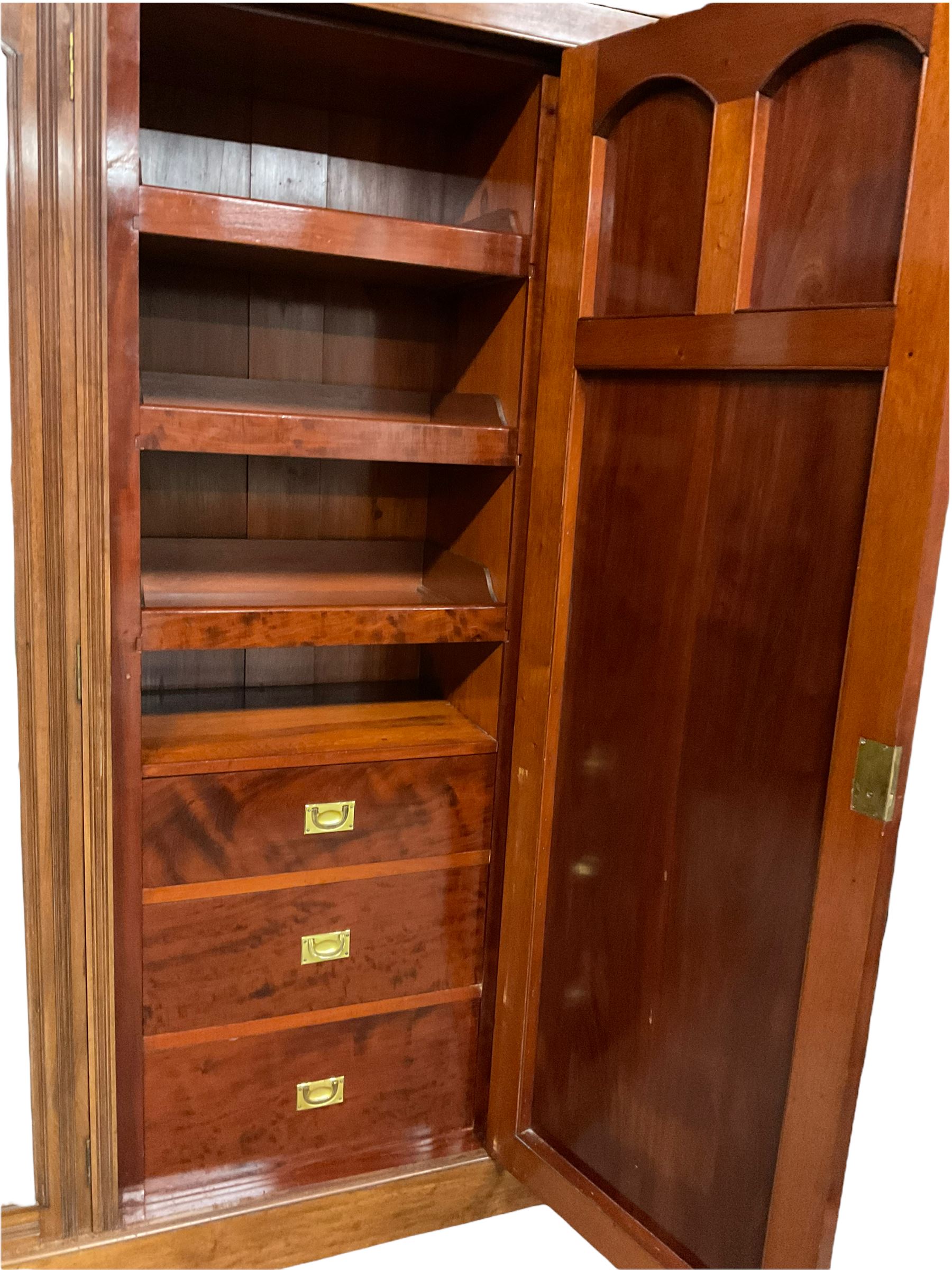 Victorian mahogany triple wardrobe, the pediment relief carved with urn and linen swags, the central panelled door carved with two fan motifs enclosing slides and drawers, two mirror glazed doors with bevelled plates enclosing hangings space and drawers, plinth base