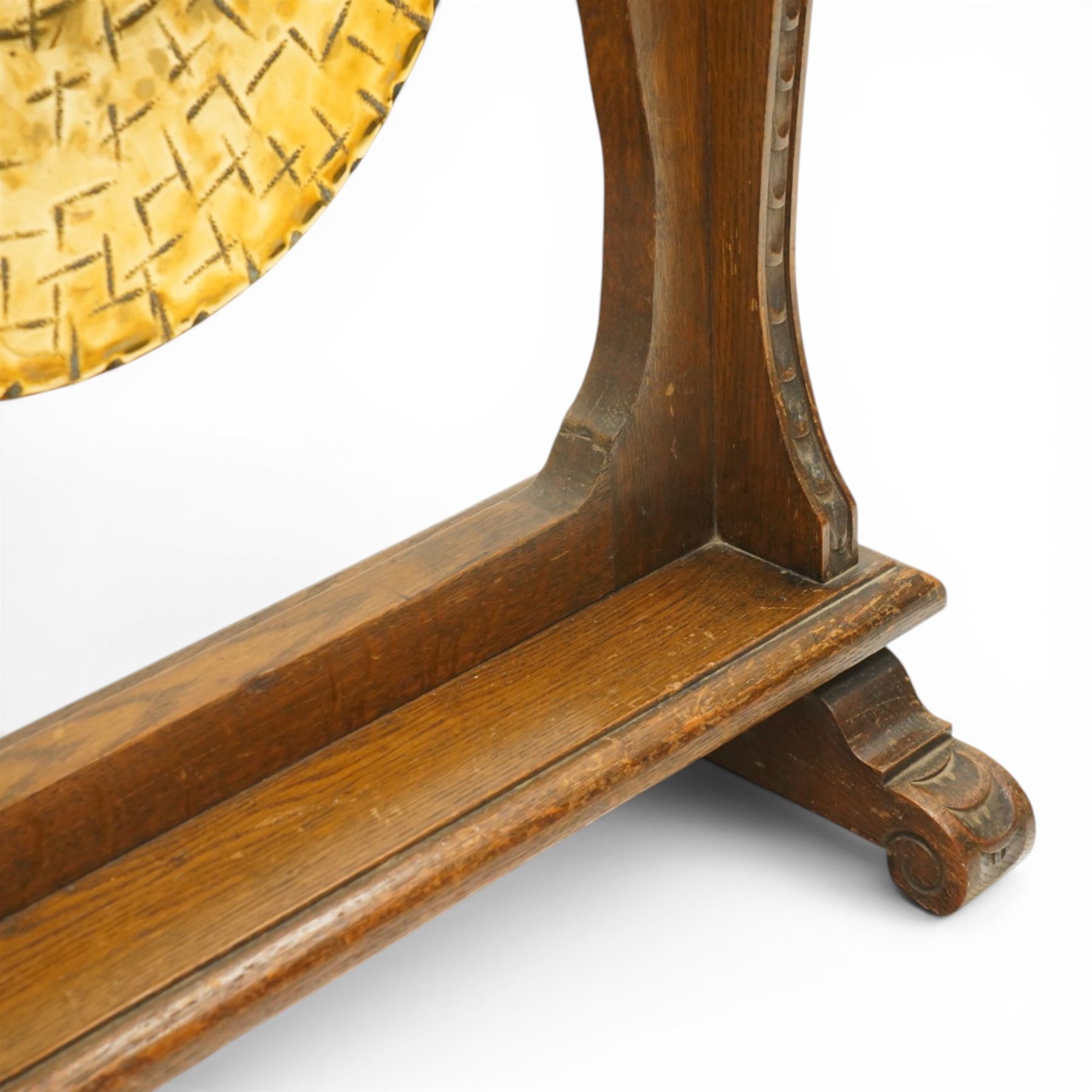 Late Victorian Arts & Crafts carved oak framed floor standing dinner gong, the cresting rail carved with central urn and trailing foliage, over shaped end supports decorated with graduating tulip and floral motifs, on rectangular base with scroll sledge feet, the brass gong stamped with William Suckling of Birmingham 'Burmese' makers mark, with striker