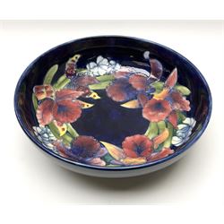 A large Moorcroft bowl decorated in the Iris pattern upon a dark blue ground, with impressed and painted marks beneath, and paper label detailed Potters to the late Queen Mary, D30.5cm.