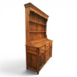 Traditional oak dresser with plate rack in the manner of Titchmarsh & Goodwin, plate rack with projecting cornice and shaped and pierced frieze, tongue and groove back three racks, over seven small spice drawers, the lower section with three short drawers, central bank three of drawers, fielded panelled sides and cupboard doors, raised on stile supports