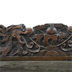 Early 20th century Chinese export carved hardwood writing bureau, the sloped fall front deeply carved with a narrative figural scene beneath pine and prunus trees, above a pair of rectangular carved panels, the shaped crest rail with entwined dragons, interior fitted with pigeonholes and a central drawer, on figural front supports with shaped stretcher