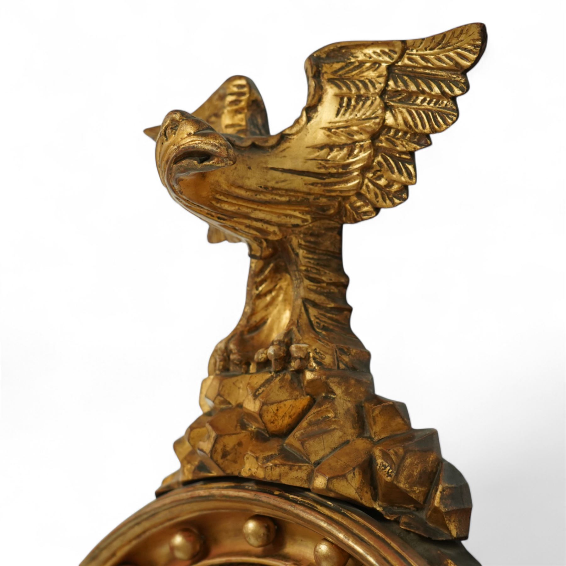 Regency period eagle mounted giltwood convex mirror, surmounted by a finely carved giltwood eagle standing on rocks above the circular mirror with the original mirror plate and surrounded by a fluted ebonized slip and the convex frame with gilt ball decorations, the back with label for ‘T.G. Woof Ltd, manufacturing cabinet makers, Devonshire Street, Sheffield