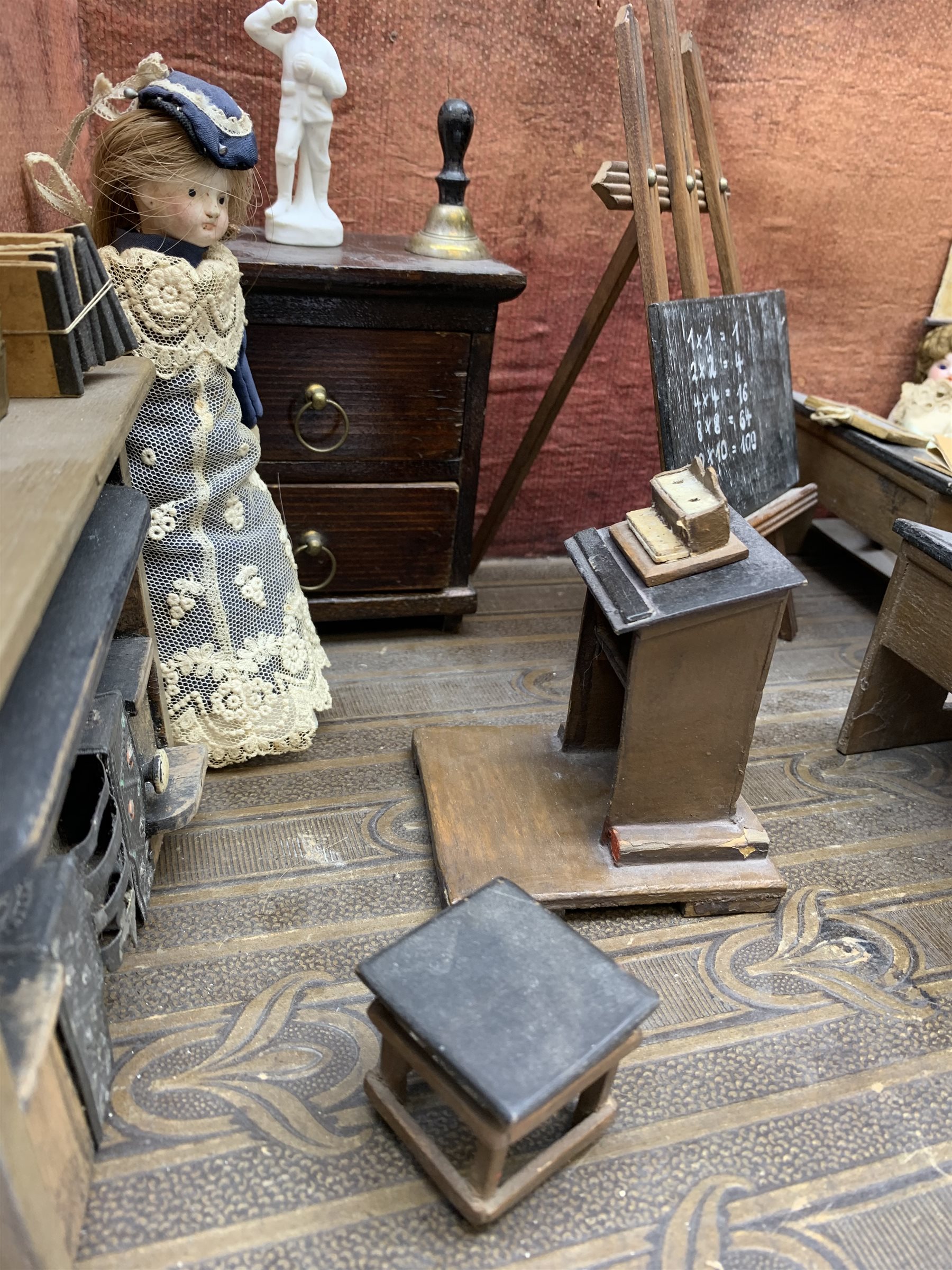 Late Victorian wooden school room setting with bisque head teacher and six German all bisque pupils each seated at a combined desk and chair with slate board, in a classroom furnished with chest of drawers, fire-surround, lectern, wall map, pictures, miniature books, school bell, chalk board on easel, wall clock etc, L70cm H28cm D28cm