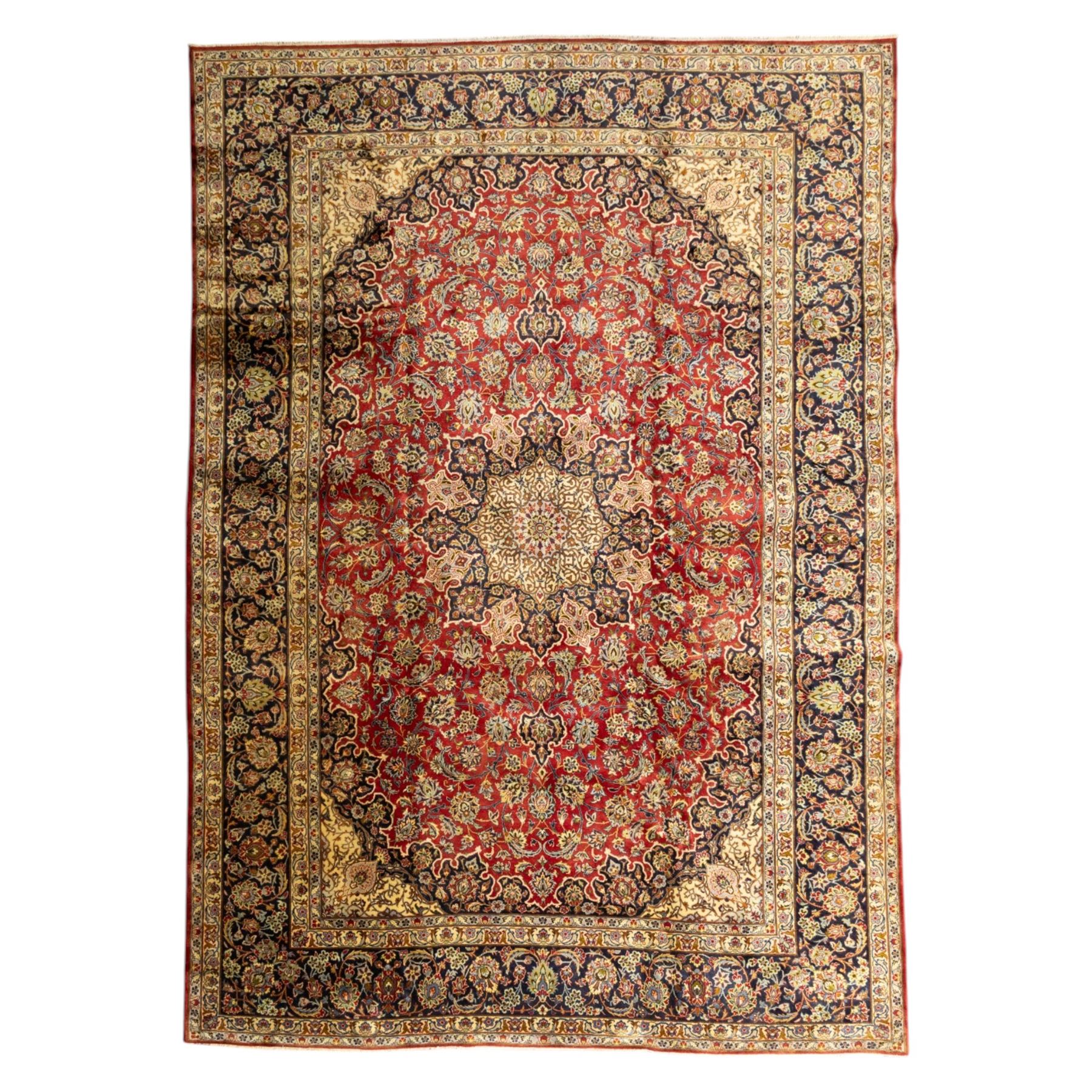 Central Persian Kashan hand-knotted carpet, crimson ground, with a large central ivory and dark navy floral medallion with pendants, surrounded by dense scrolling foliate and floral motifs incorporating rosettes, palmettes and vine work, enclosed by ivory spandrels and a dark navy border with repeating palmettes and meandering vines, flanked by floral guard stripes