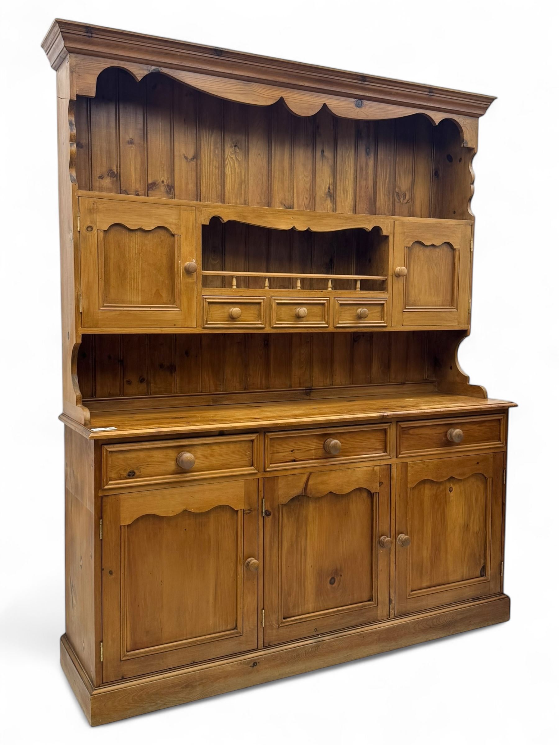 Traditional vintage pine kitchen dresser with scrolled cornice and rack with long shelf above a galleried shelf flanked by three short drawers and two cupboards, the base with three long drawers above three cupboards on plinth base  
