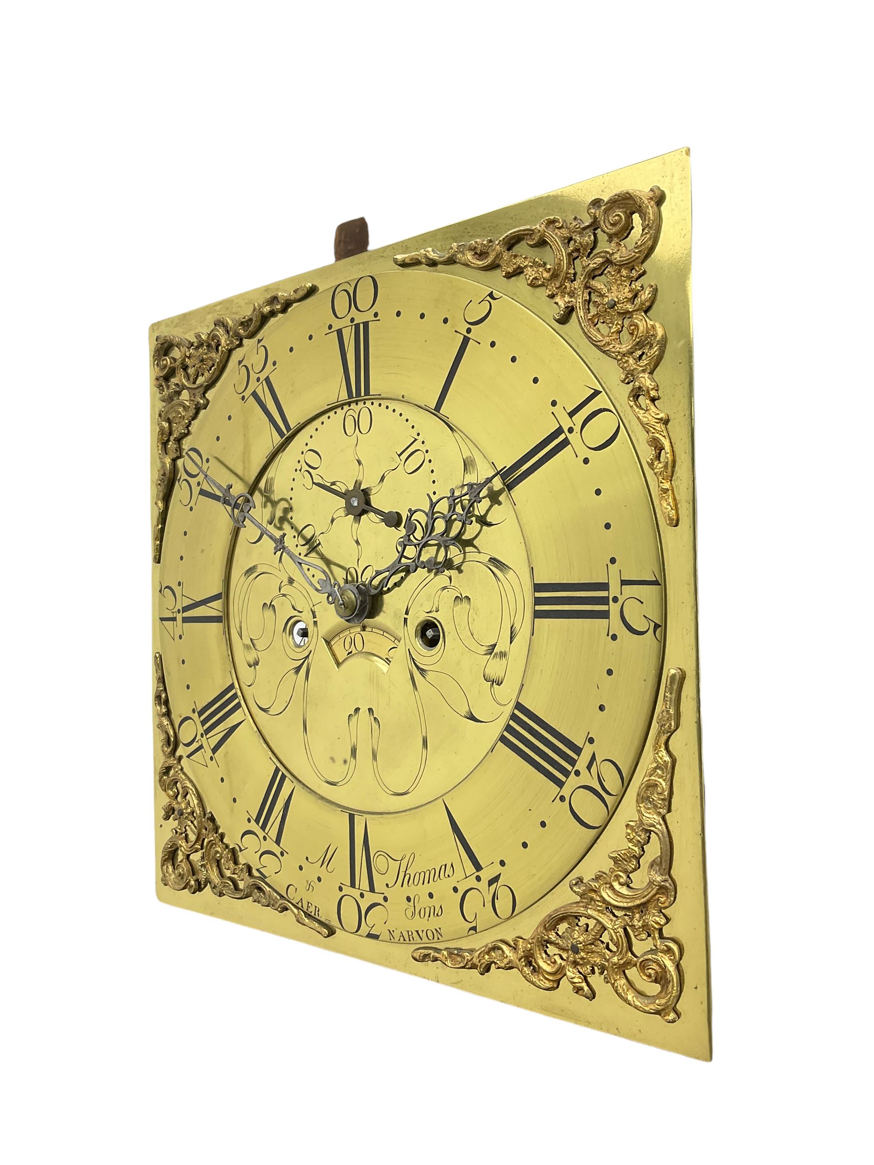 An 18th century oak cased longcase clock by M Thomas & Sons, Carnarvon c1780, flat topped hood with a wide cornice and plain frieze, glazed hood door flanked by two shaped pillars, with a long trunk and  door with a break arch top, with canted and reeded corners on a short plinth with a raised conforming break arch panel and skirting, 13” brass dial with an engraved centre,  small semi-circular date aperture and disc behind, with a subsidiary seconds dial, non-matching steel hands and scroll spandrels, Engraved chapter ring with roman numerals, five minute Arabic's and minute markers, dial pinned directly to an eight day rack striking movement, striking the hours on a cast bell. With weights, pendulum and key.    
Michael and Morris Thomas are recorded as working together in Carnarvon 1769-94.




