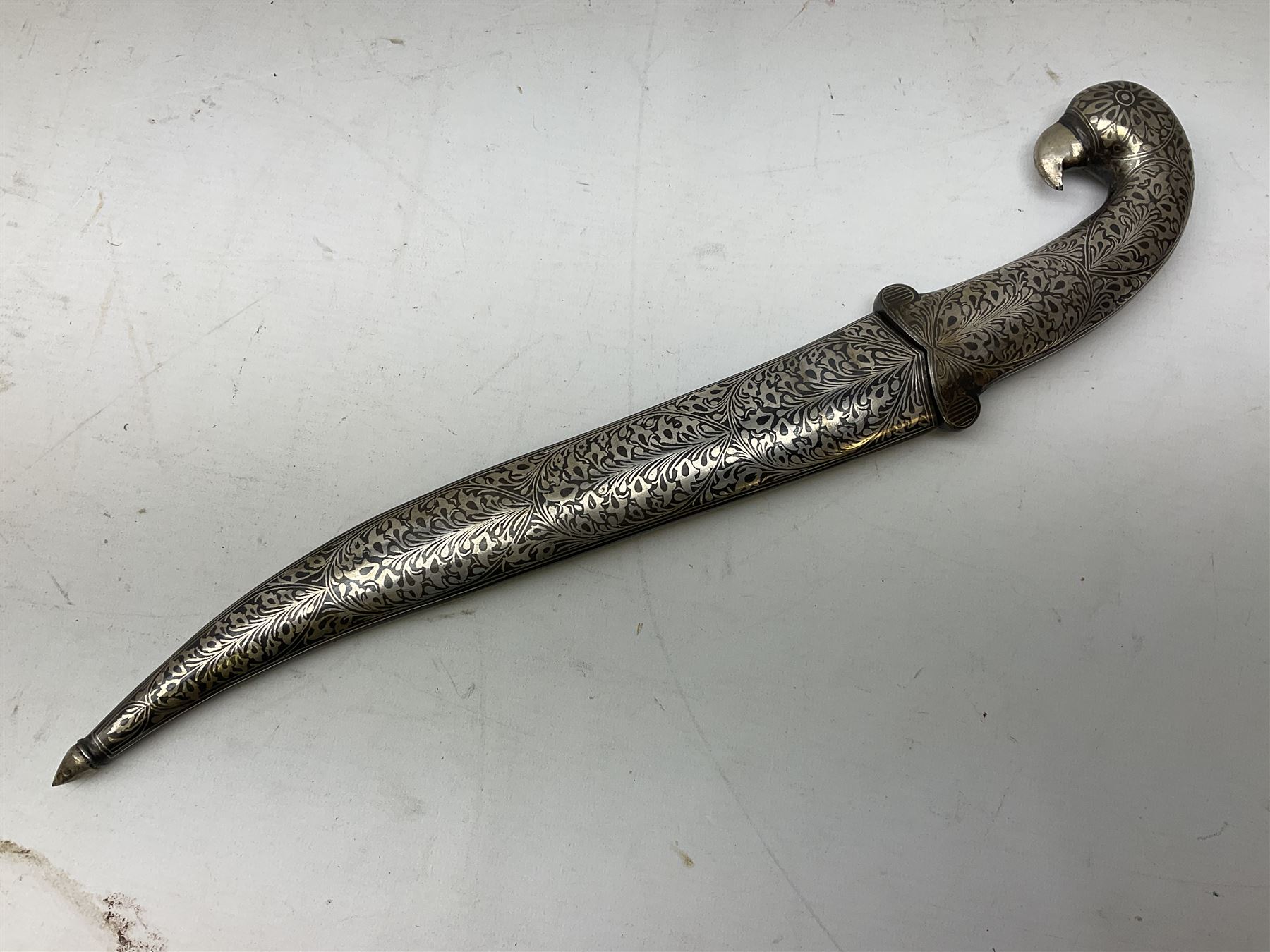 Indian Khanjar dagger with 28cm curving damascus steel blade inlaid with silver floral emblem, white metal and niello style grip in the form of a bird's head with pronounced beak and matching scabbard L44cm overall