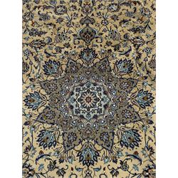 Central Persian Kashan pale khaki and ivory ground carpet, shaped central medallion enclosing small stylised motifs, the field decorated profusely with trailing foliate branches and plant motifs, guarded border with repeating floral design