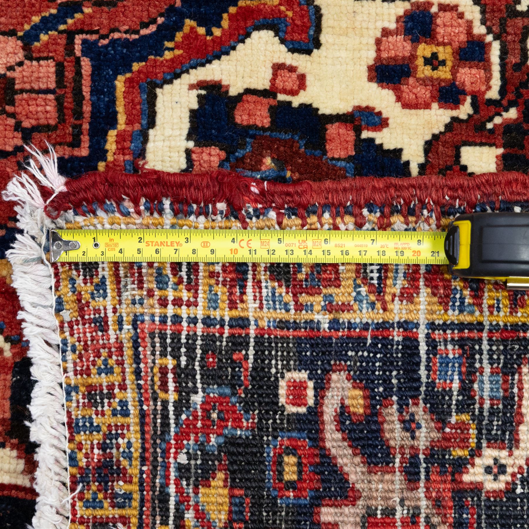 North West Persian Ahar hand-knotted carpet, red field with large central angular star medallion with stepped outlines and radiating geometric motifs surrounded by stylized floral and serrated leaf forms, enclosed by a deep blue main border decorated with angular palmettes and rosettes flanked by multiple guard stripes, with cotton fringe ends 