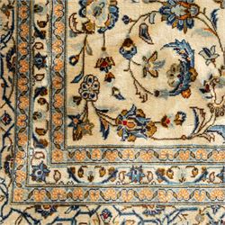 Central Persian Kashan rug, cream ground densely patterned with interlaced floral stems and rosettes in blue, gold and brown, framed by layered borders featuring stylised palmettes, woven in the Kashan weaving district of Iran