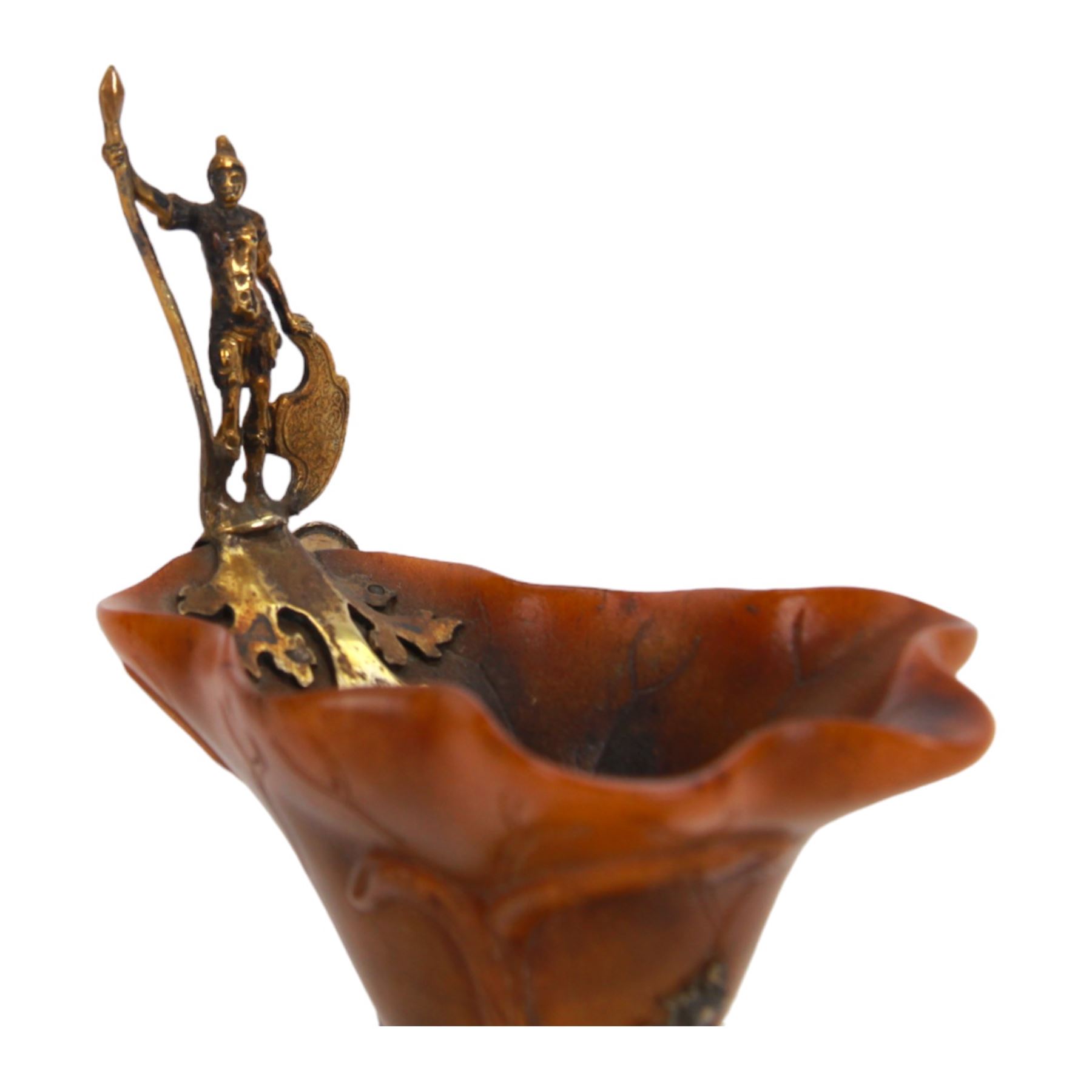 Rhinoceros horn libation cup with gilt metal mounts, probably 18th century, the cup of naturalistic form carved with veins, with gilt figural handle, upon a gilt knopped stem and quatrefoil base embossed and chased with trophies and foliate motifs, H14.5cm
