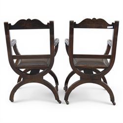Late 20th century stained beech Savonarola chair, the carved crest rail and open arms above an upholstered leather seat, raised on an X framed base with carved foliate and mask decoration, joined by turned stretcher and ending in castors