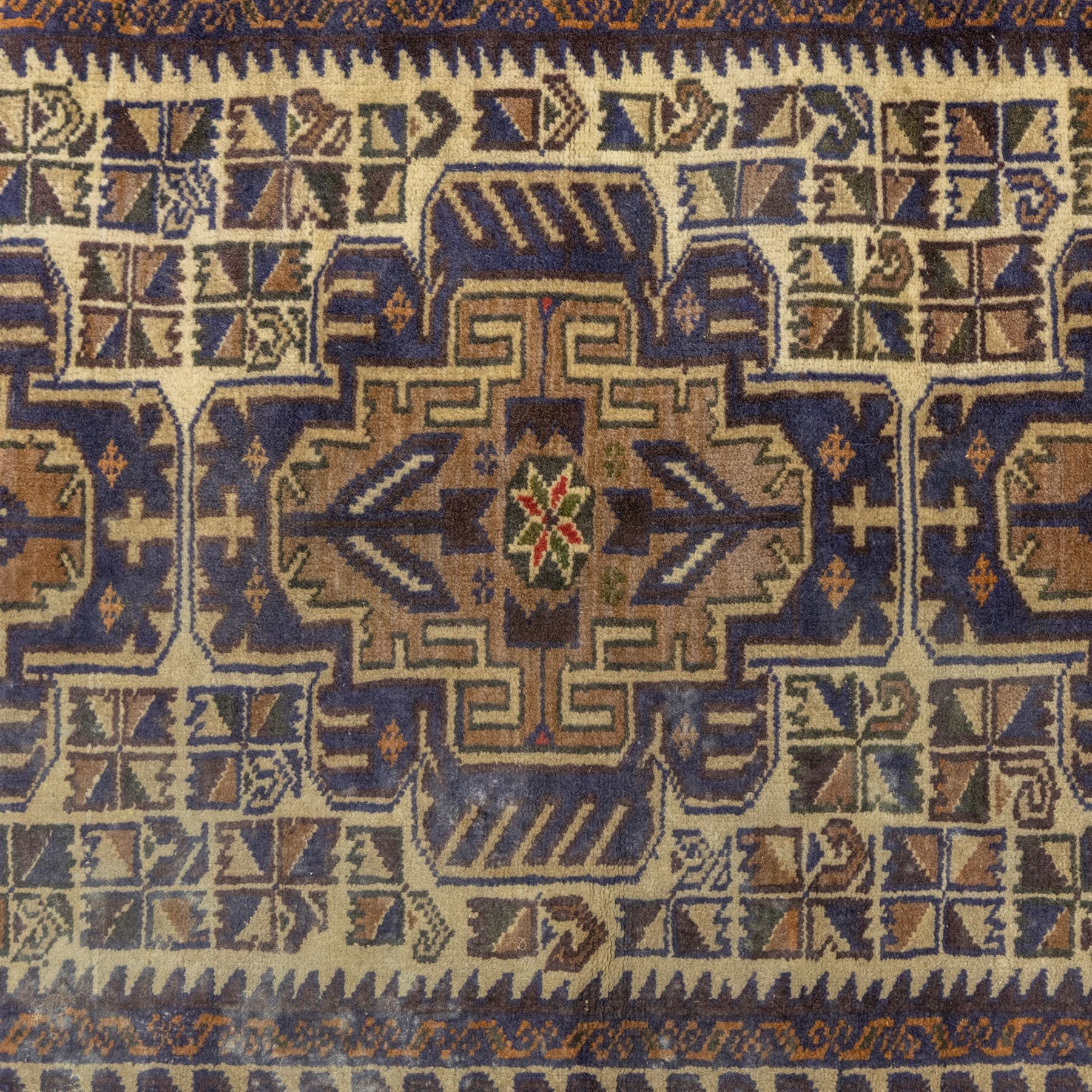 Baluchi design wool rug, with three geometric medallions on a cream field, enclosed by multiple dark blue, brown and rust geometric borders with fringed ends