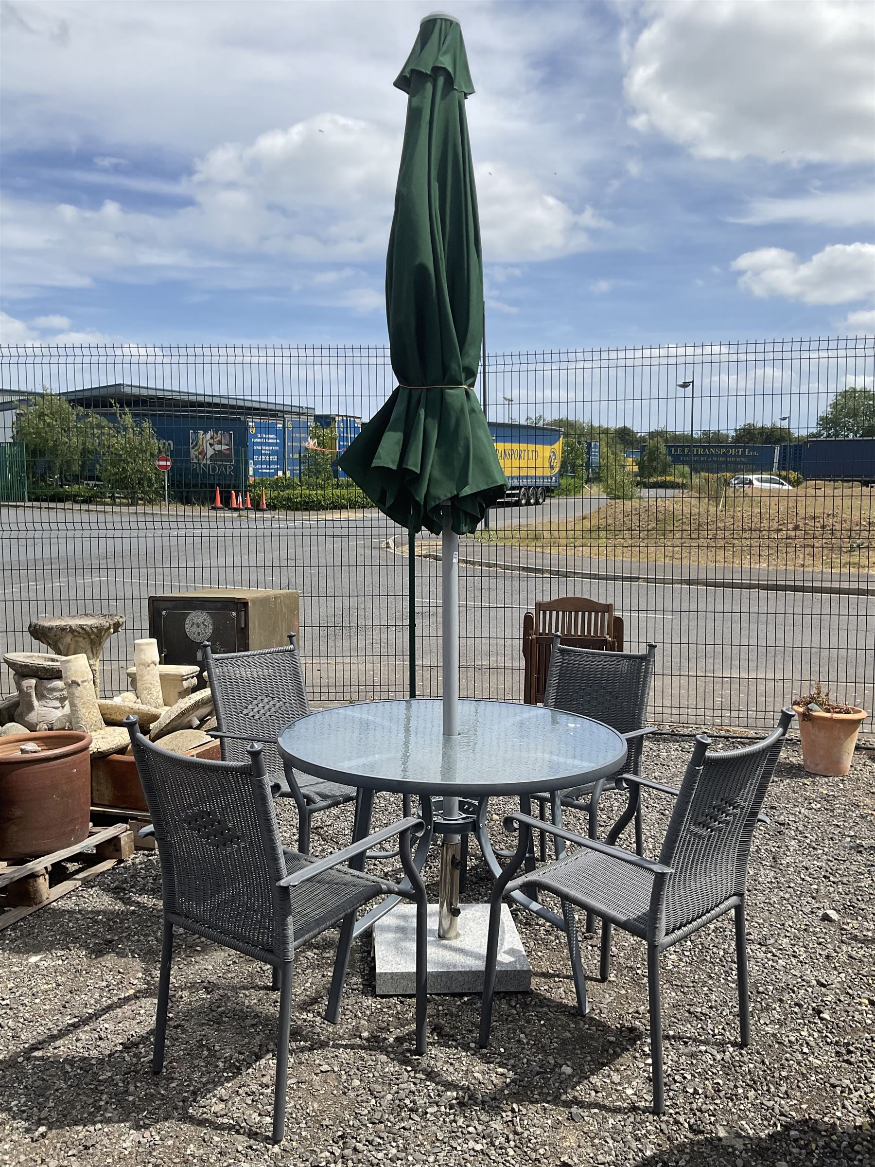 Grey aluminium circular glass top garden table, and four chairs with parasol on granite base