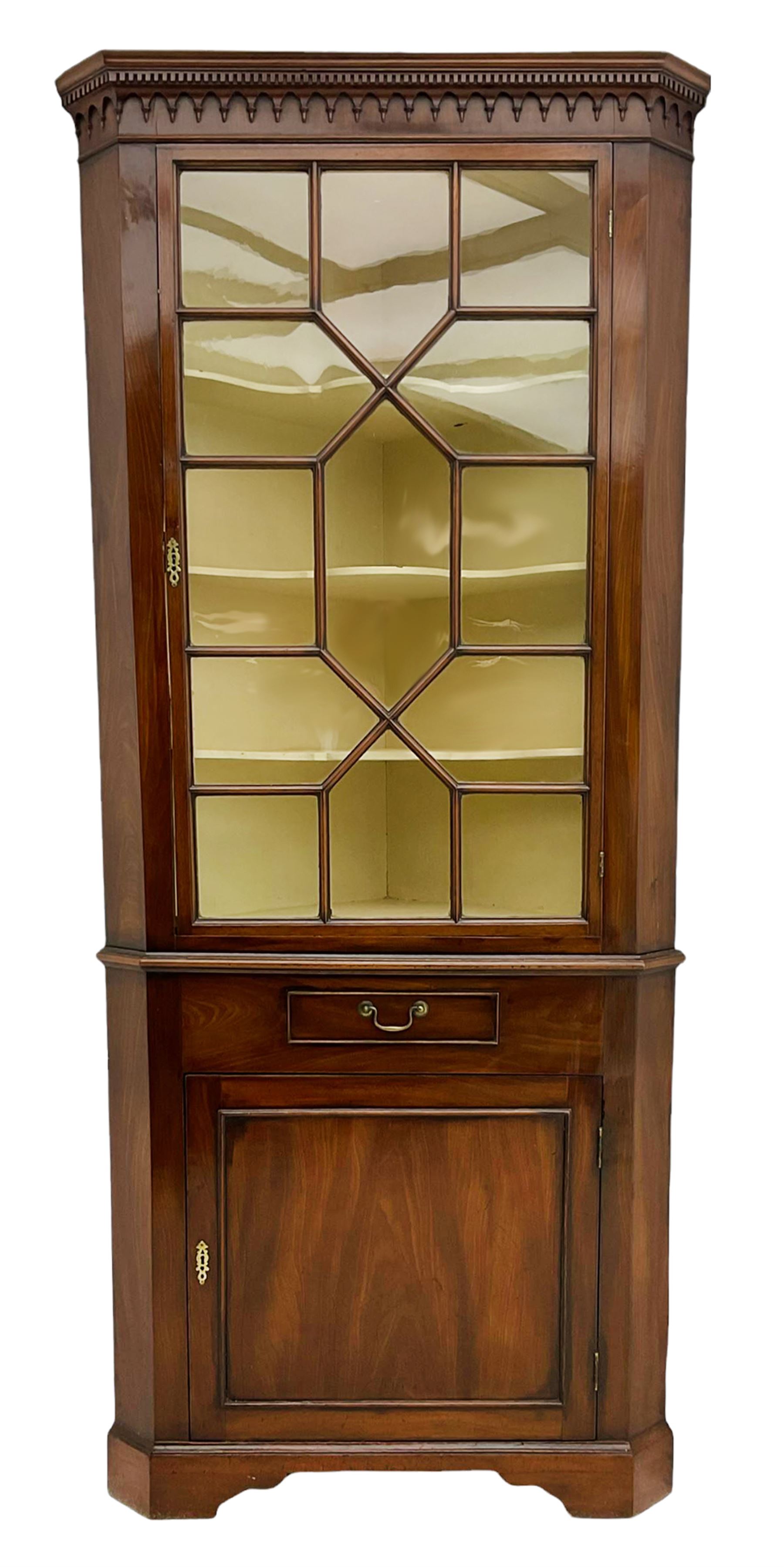 George III mahogany floor standing corner display cabinet, dentil cornice, upper astragal glazed door above small drawer and lower cupboard, on bracket feet, in two sections
