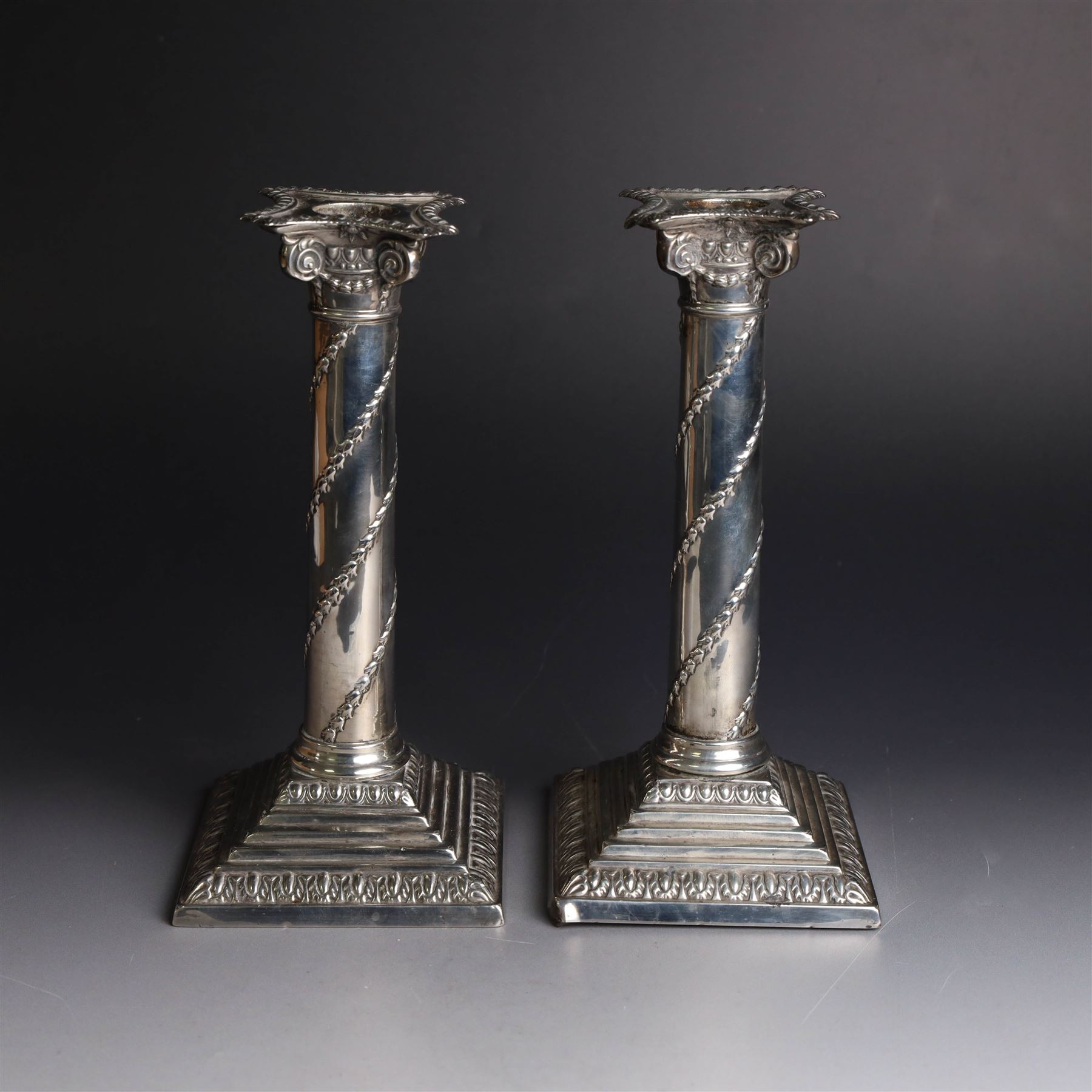 Pair of Edwardian silver mounted column candlesticks, each with embossed floral, foliate and scrolling decoration and upon stepped square weighted bases, hallmarked William Hutton & Sons Ltd, London 1901, H19cm