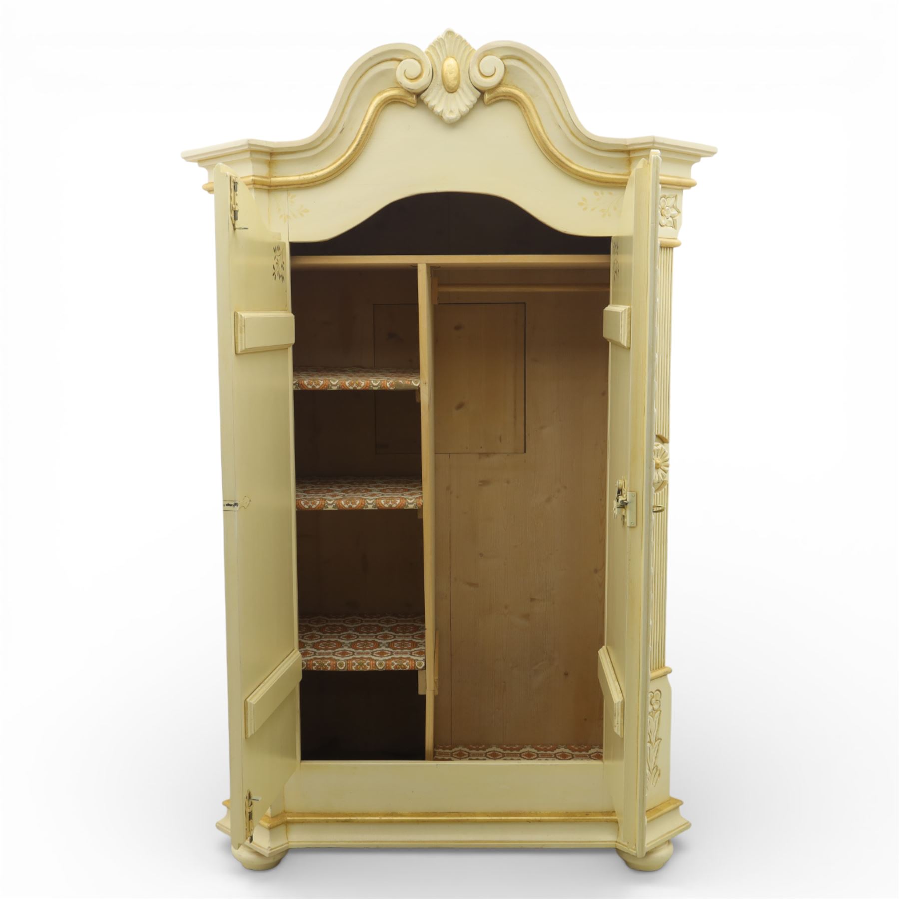 20th century French white and parcel gilt painted armoire, the shaped and scroll moulded cornice centred with a stylised foliate, the double doors with raised panel reserves applied with gilt foliate scrollwork, flanked by fluted pilasters with floral capitals, opening to a fitted interior with shelving and hanging space, raised on a moulded plinth on squat bun feet