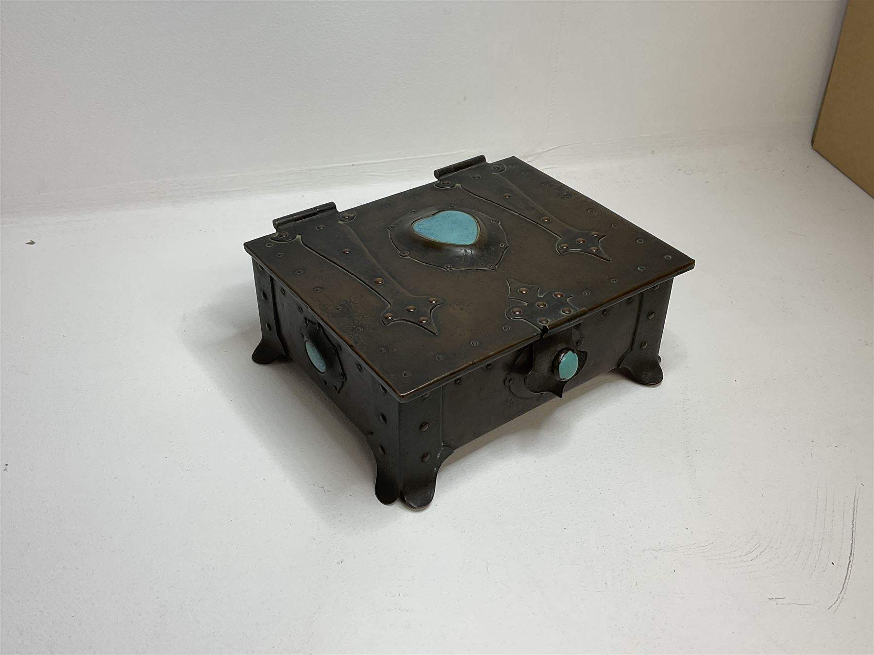 Arts and Crafts copper box, the lid decorated with stylised riveted hinges and inset with Ruskin type ceramic turquoise heart-shaped cabochon, the mount etched M.B 1913, and further cabochon roundel to each side panel, including one inset to the clasp acting as the knob to the locking mechanism, marked RS Douglas 1913 beneath, W16.5cm H7cm D15cm