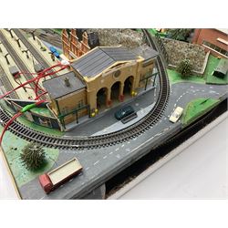 Table top 'N' gauge continental scenic layout as a split level town with various loops of track, station with numerous platforms, engine shed, assorted buildings, roads with motor vehicles and figures, tunnels, trees, river with bridge, tram depot etc 122 x 52cm