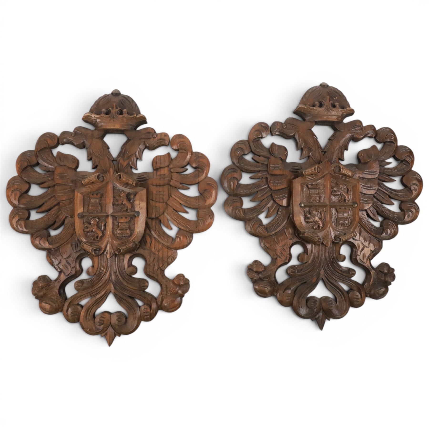 Carved wooden wall plaque, decorated with foliate scrolls, with two reproduction swords attached, together with five other wooden plaques with foliate scrolls and shields