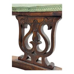 Late Victorian carved mahogany open armchair, the shaped back with fluted upholstered panel and padded arms above pierced scroll carved side supports, over a broad upholstered seat, on turned front supports