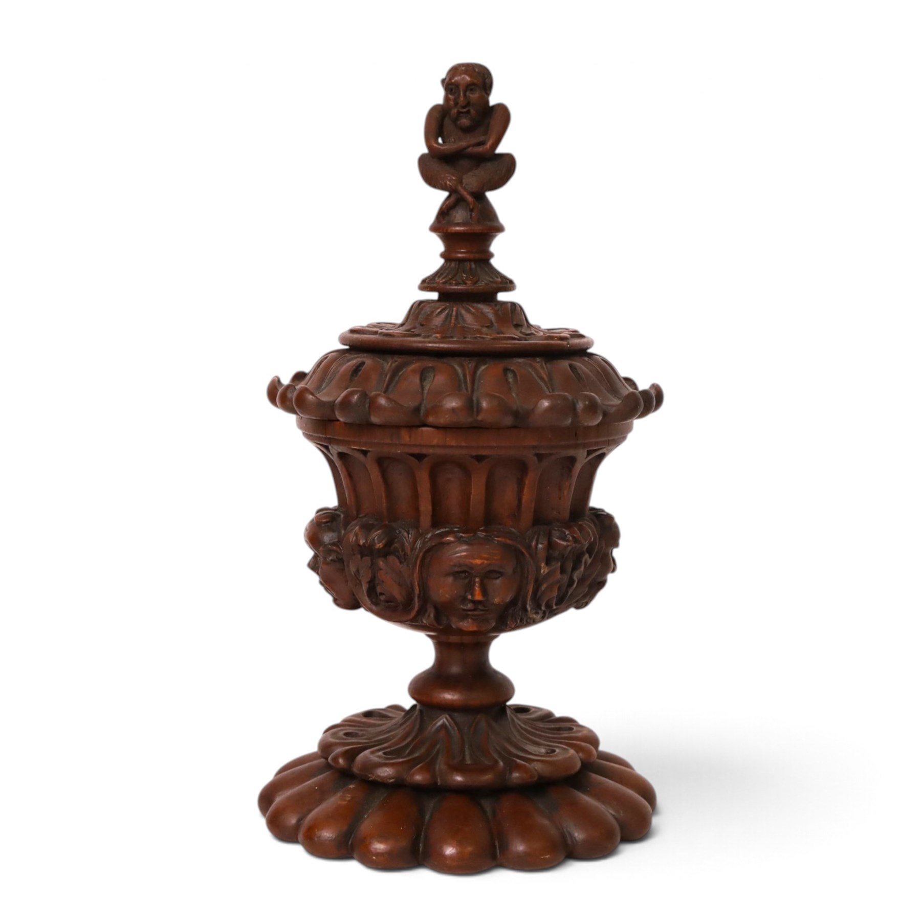 Carved wooden urn. decorated in relief with carved faces within foliage, with a Satyr finial, H25cm 
