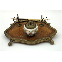 A 19th century desk stand, the porcelain inkwell painted with floral sprigs and heightened with gild, and cover with bud finial, before a quill or pen support, set upon a shaped metal mounted base and raised upon four bud modelled feet, L20cm.