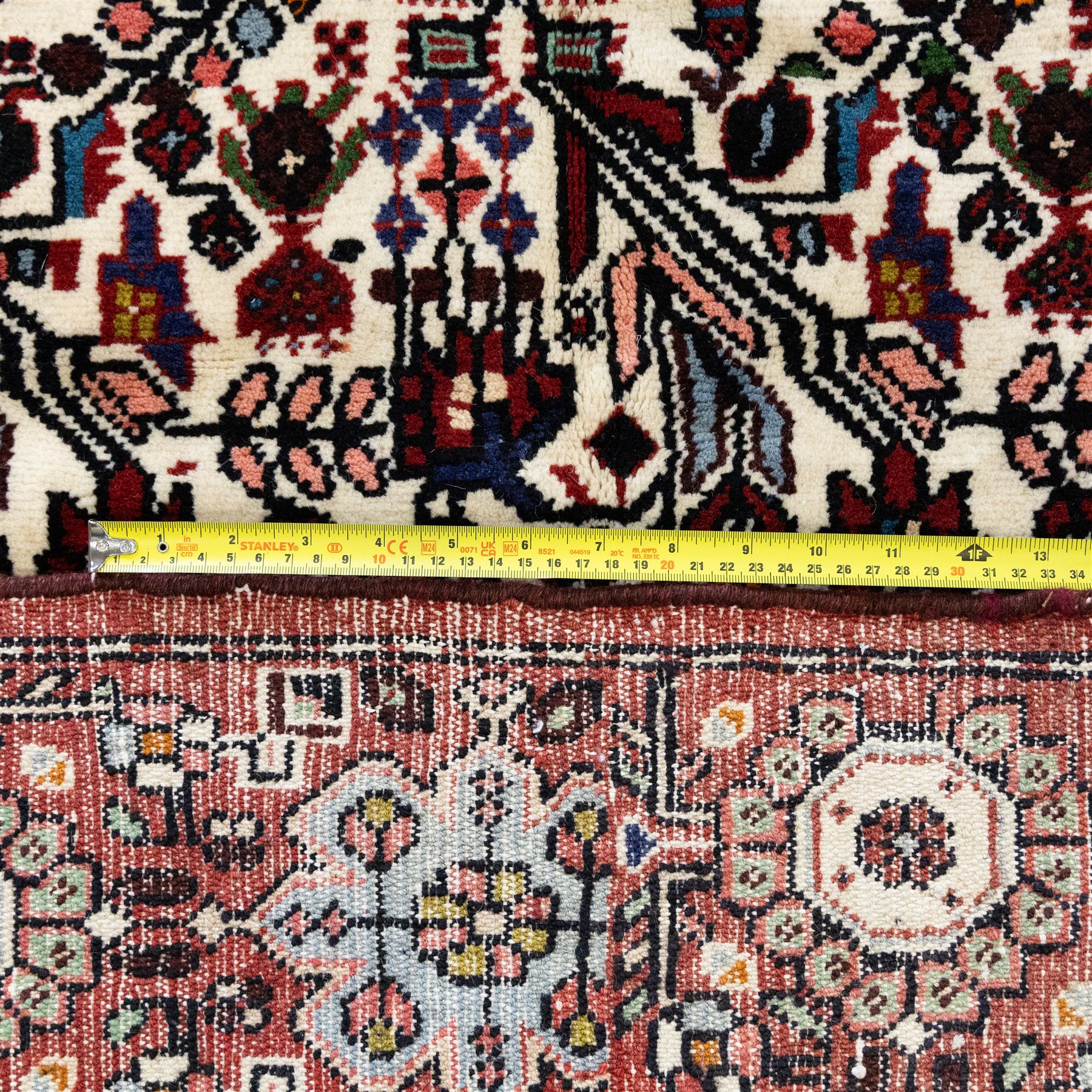North west Persian Rudbar hand-knotted rug, ivory field woven with a repeating pattern of stylized shrubs, rosettes, and geometric floral motifs in tones of madder red, turquoise, indigo, and ochre, enclosed by a border of linked rosettes and angular flowerheads between narrow guard stripes 