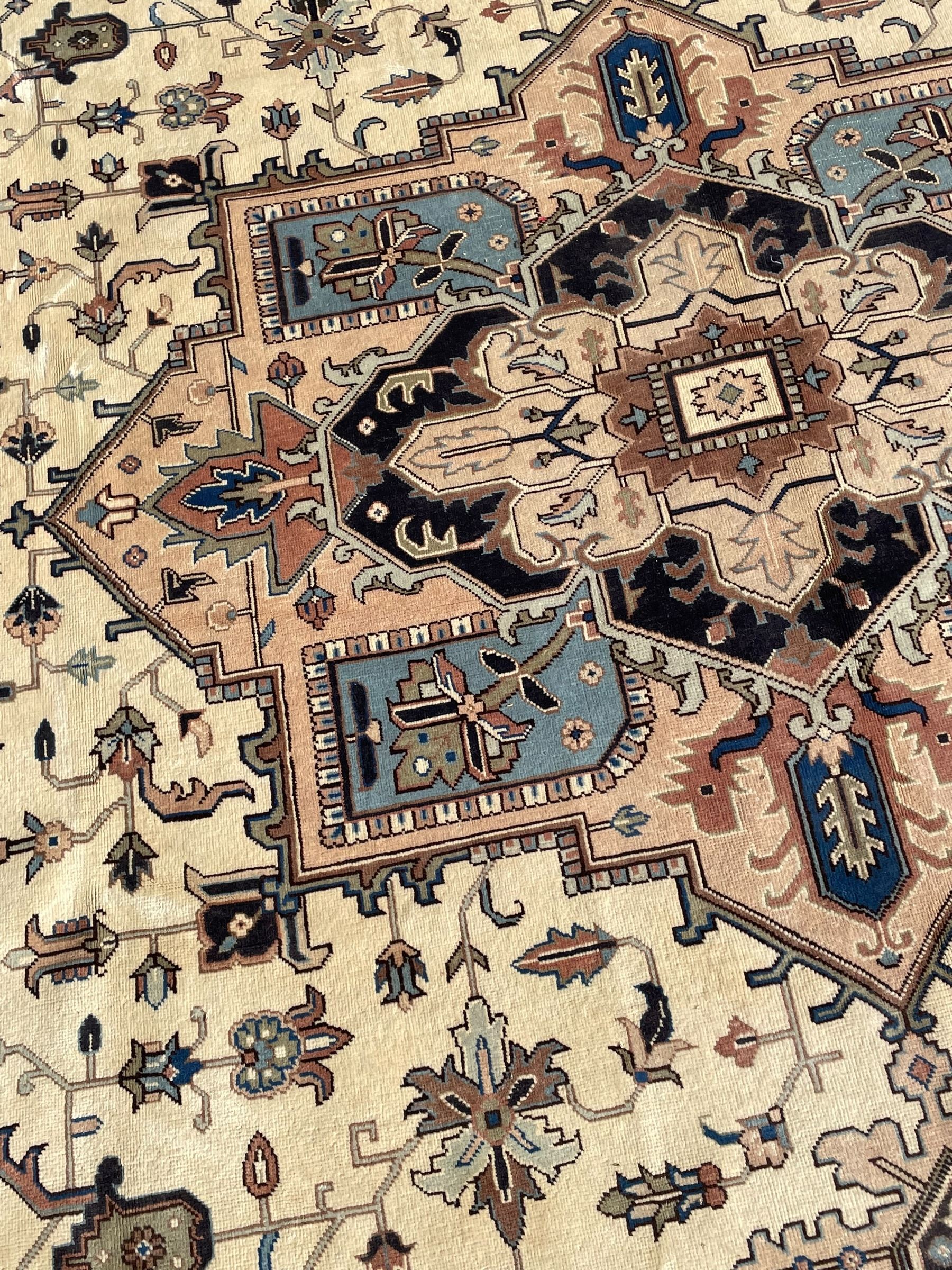 Persian Heriz pale olive and ivory ground carpet, large quatrefoil medallion with palmettes, the surrounding field decorated with trailing leafy branches and stylised plant motifs, peach ground borders with overall floral pattern, within guard stripes 