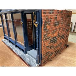 Good quality late 20th century dolls house by M. James dated 1995 in the form of a Beverley East Yorkshire Antique Shop called 'North Bar Antiques'; single-storey single-roomed shop with textured brick walls and flat roof, fully glazed hinged front with recessed hinged customer door and central window to the rear; comprehensively furnished with chests of drawers, pedestal desk, breakfast table, lowboy, two longcase clocks, delft rack with ceramics, occasional tables, pictures, Regency style mirror and collectibles; decorated walls with coving and picture rail and simulated floorboarding; wired for electric lighting; maker's plaque W61cm H42.5cm D41.5cm