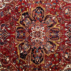 North West Persian Ahar hand-knotted carpet, madder red ground, with a large central shaped floral medallion with pendants, surrounded by angular scrolling foliate motifs incorporating rosettes, palmettes and stylised flowerheads, enclosed by ivory spandrels and a dark navy border with repeating geometric floral motifs and meandering vines, flanked by narrow patterned guard stripes, with cotton fringes