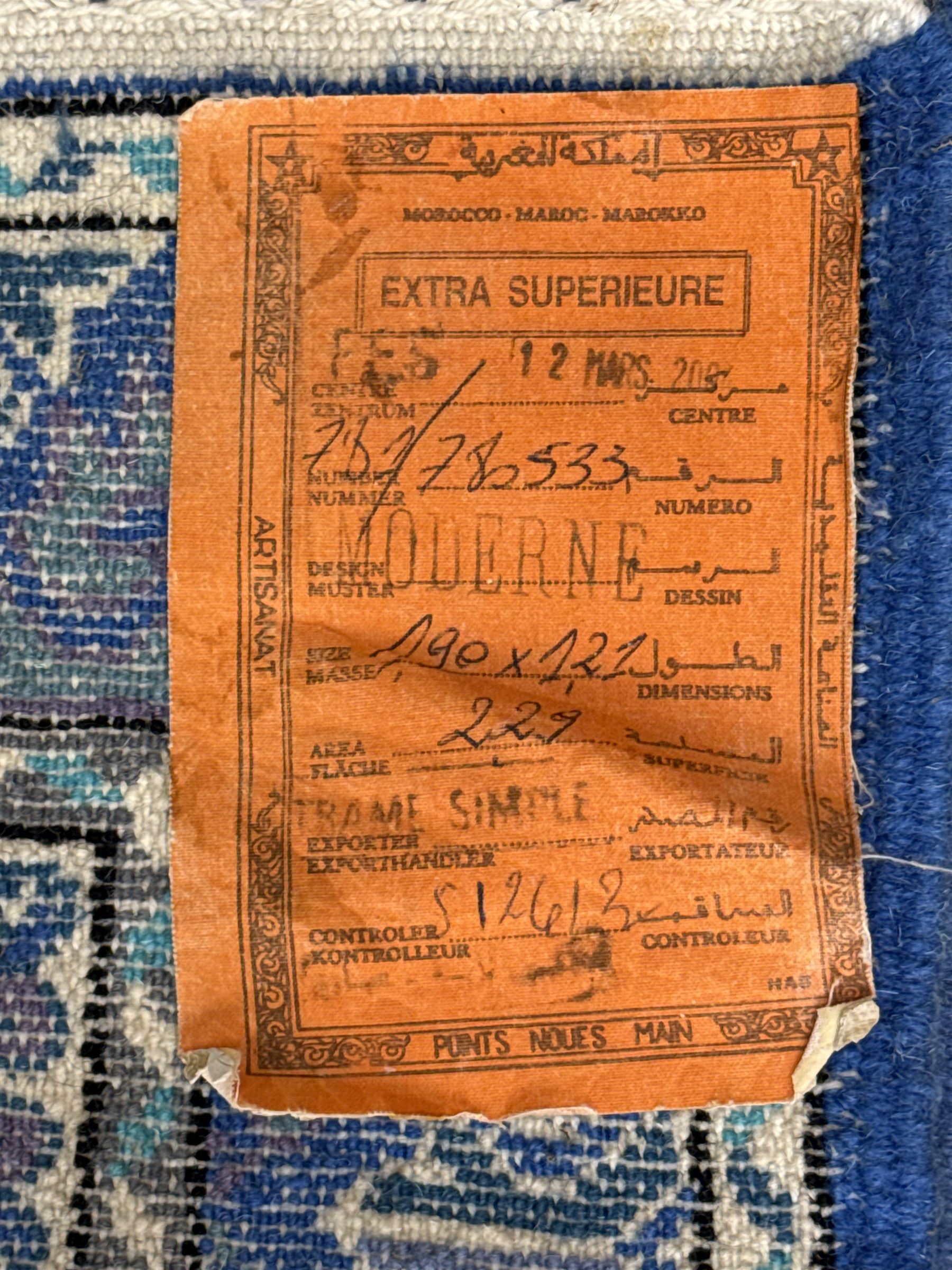 Morrocan single weft blue ground rug, the field segmented into a grid of ten rectangular panels, bordered by a series of guard bands with repeating floral and geometric patterns with interlocking vines and rosettes, the edges finished with a fringe of twisted tassles