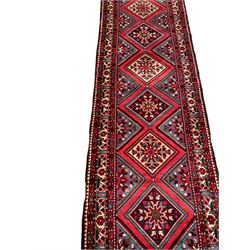 Persian Hamadan runner, red ground, decorated with eighteen lozenge medallions decorated with stylised floral motifs, three band border decorated with plant motifs and geometric patterns