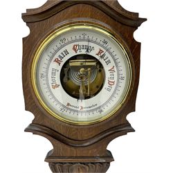 A carved oak cased aneroid barometer c1950 with an 8” open enamel dial,  recording air pressure from 26 to 32 inches with weather predictions in contrasting gothic script, with a steel indicating hand and brass recording hand within a brass bezel and flat glass, boxed mercury thermometer recording the temperature in degrees centigrade and Fahrenheit.  

