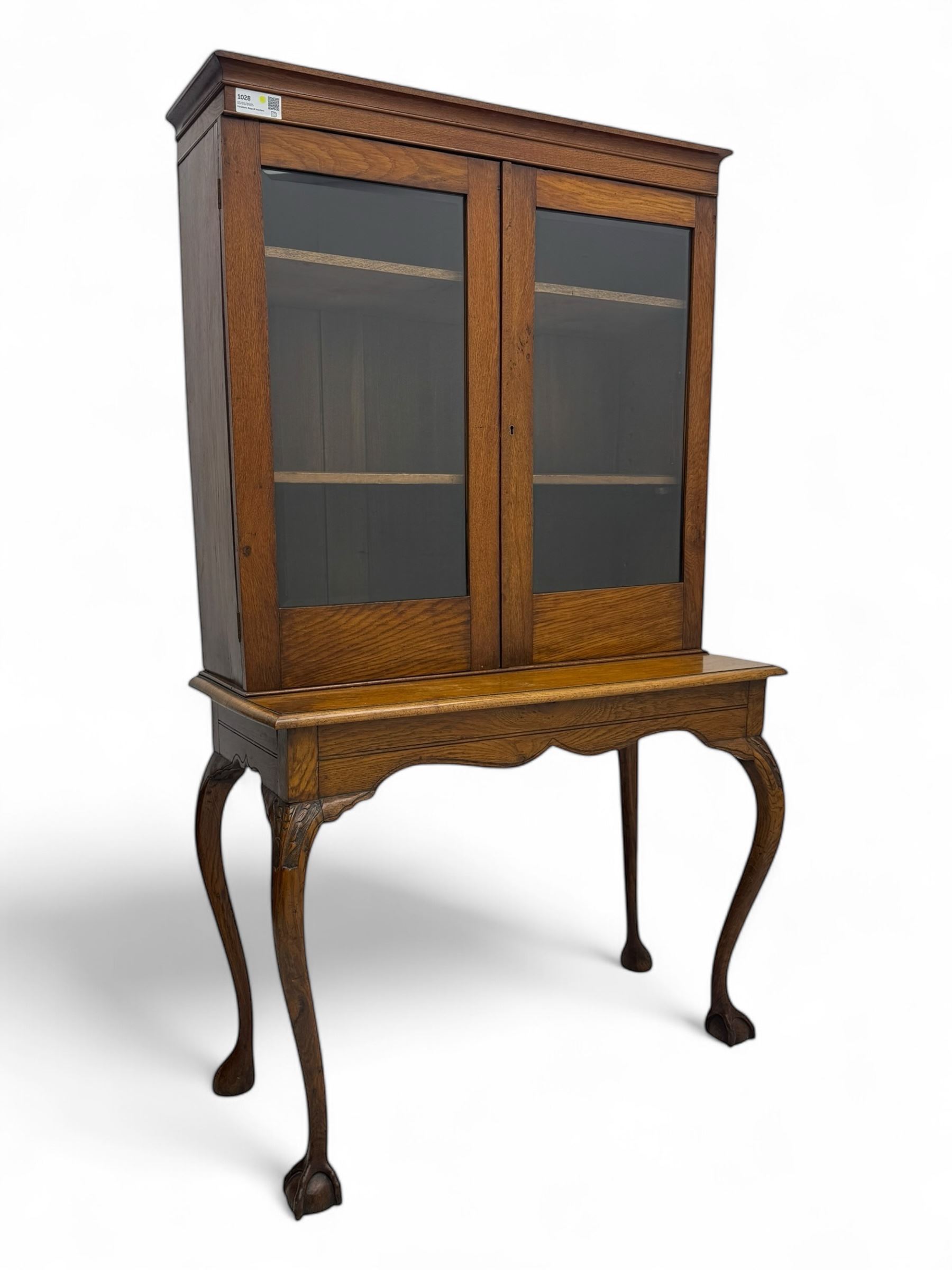 Late 19th century oak display cabinet, rectangular form with a pair of glazed doors enclosing shelves, raised on cabriole supports with carved detailing ending in claw feet