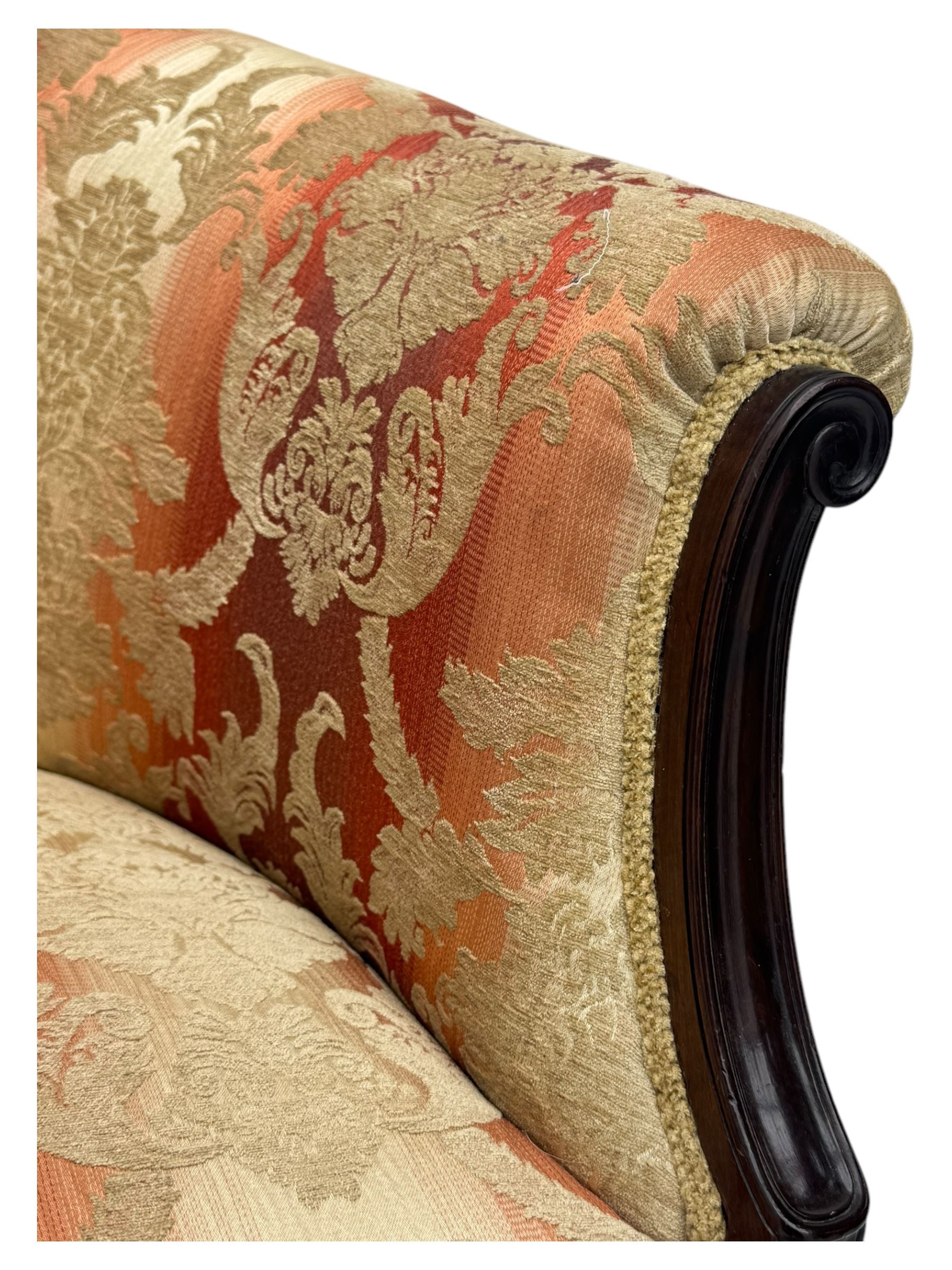 Early 20th century mahogany framed upholstered tub armchair, scrolled arms, upholstered in a damask-style fabric with foliate pattern, raised on cabriole front legs upon brass castors