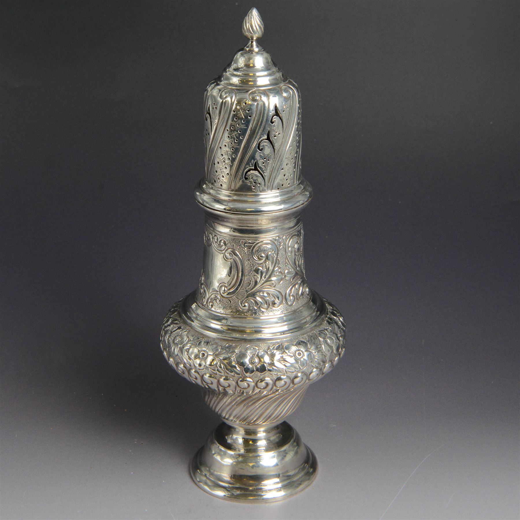 Victorian silver sugar caster, of bellied urn form, embossed with floral and foliate motifs, with two vacant cartouche, upon a domed stepped circular foot, with pierced removable cover with flambe finial, hallmarked Marston & Bayliss, Chester 1900, H25cm