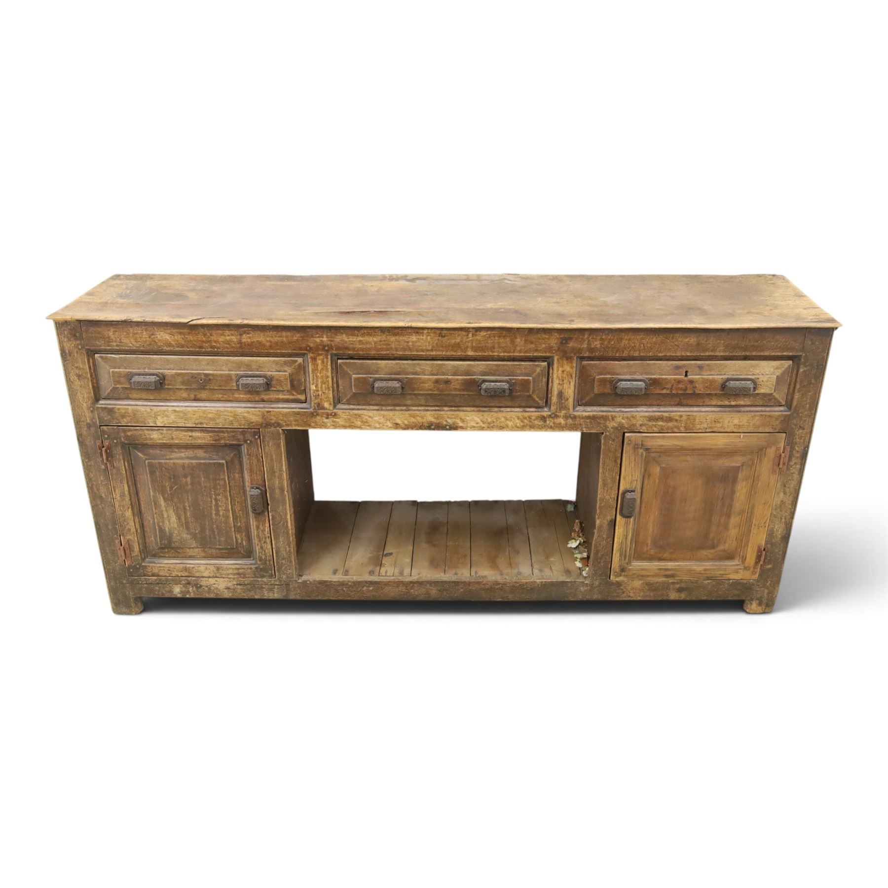 18th century rustic oak dresser base, with fielded panels and iron cup handles with embossed greek key and foliate detail, three short drawers above and open recess flanked by two cupboard doors, raised on stile supports